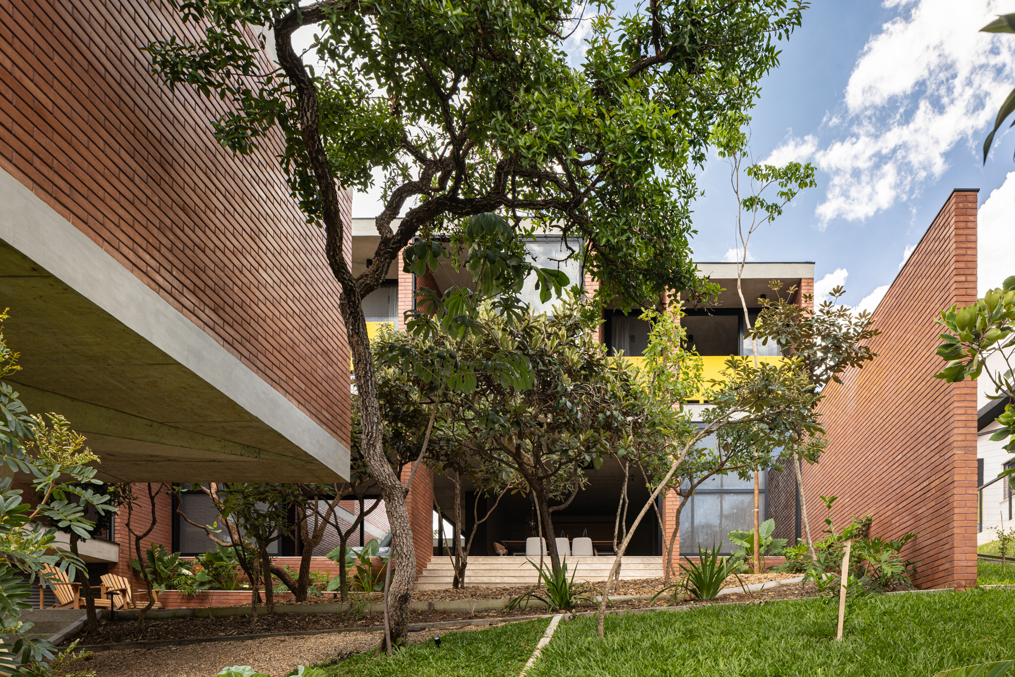 Passarela com brises metálicos amarelos conectam áreas desta casa no mato. Projeto de Hersen Mendes Arquitetura.