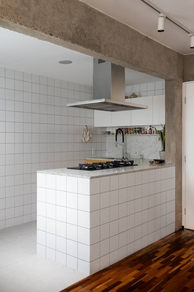 Apê tem piso de tacos reciclados e azulejos brancos pequenos na cozinha. Projeto de BLOCO Arquitetos.