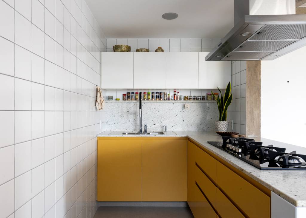 Apê tem piso de tacos reciclados e azulejos brancos pequenos na cozinha. Projeto de BLOCO Arquitetos.
