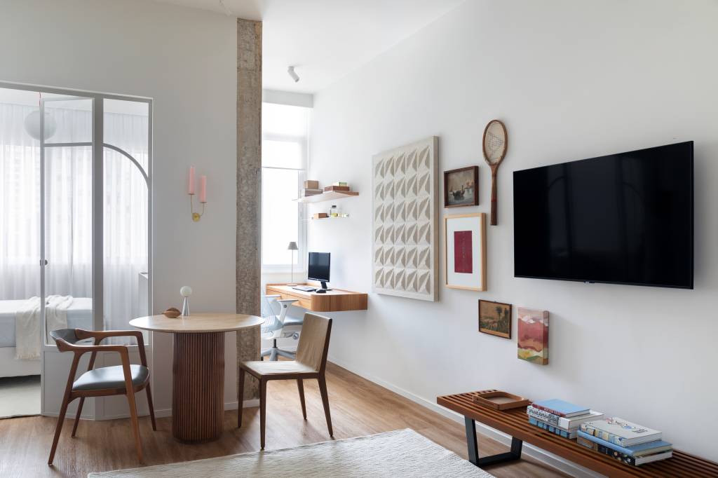 Delicada porta de serralheria branca separa quarto neste apê de 40 m²