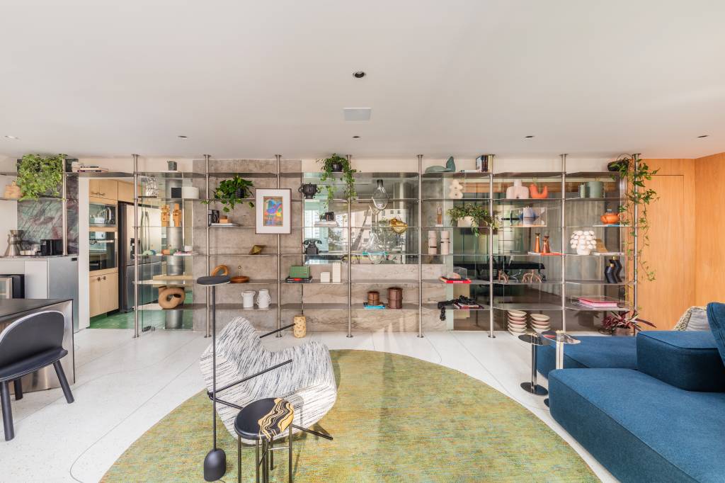 Estante em aço inox é peça que cria continuidade em área social de apê integrado. Projeto de Zalc Arquitetura.