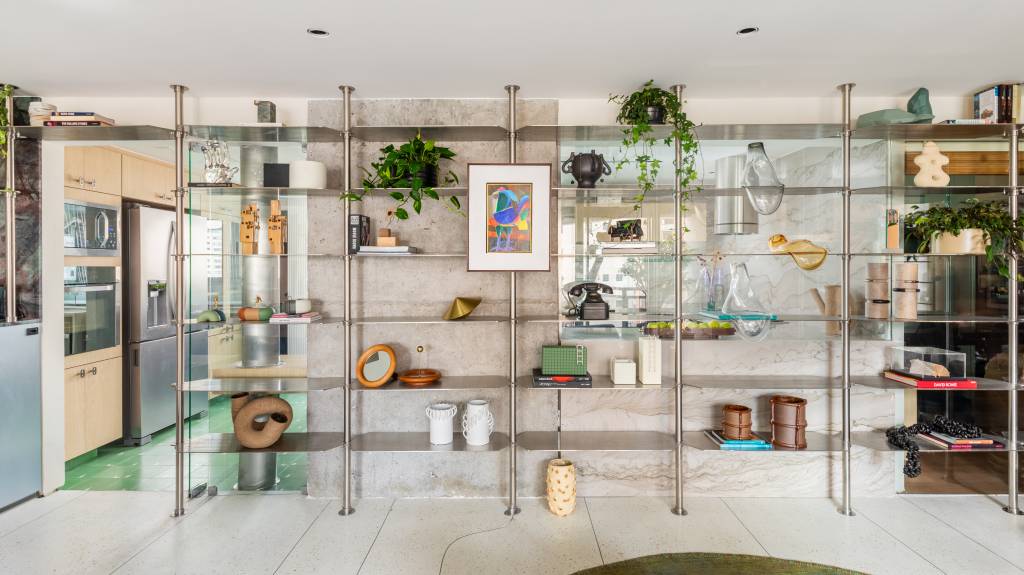 Estante em aço inox é peça que cria continuidade em área social de apê integrado. Projeto de Zalc Arquitetura.