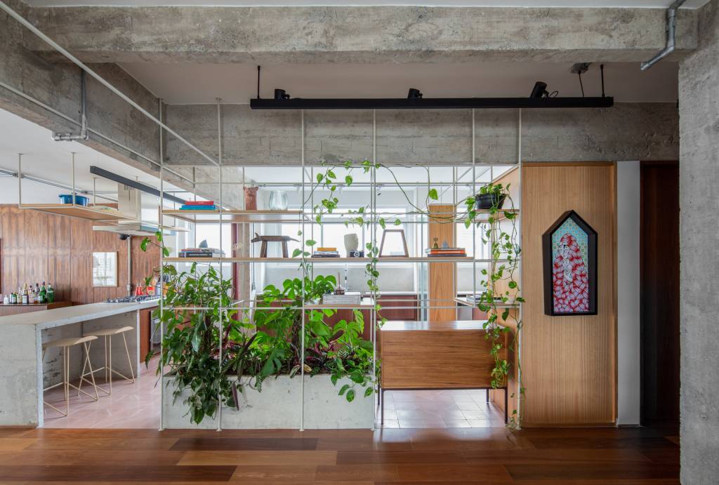 Neste apê, estante metálica branca é divisória e floreira para jiboias e costelas-de-adão