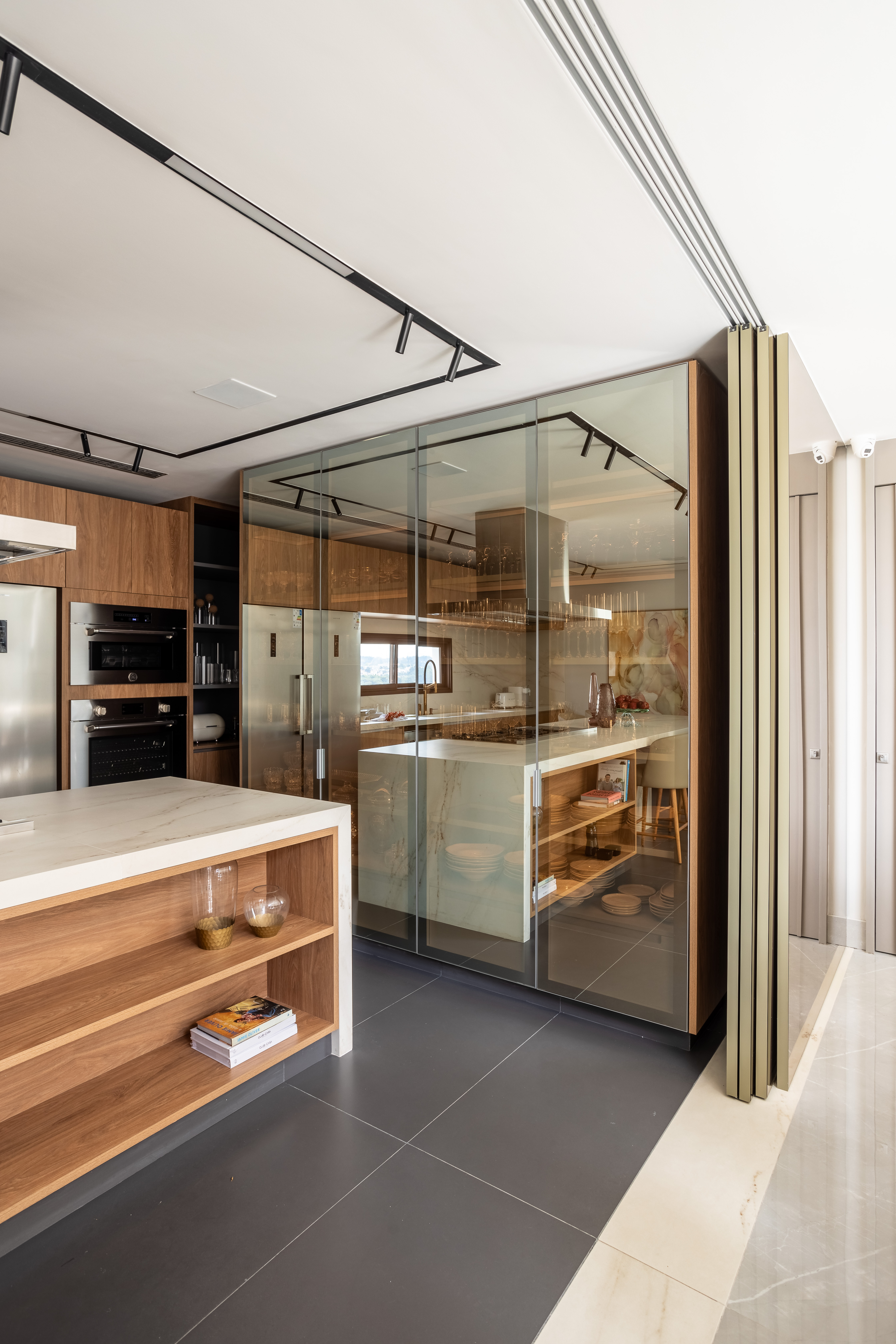 Casa na Granja Viana tem escada de porcelanato plissada, cabeceira de pedra e cristaleira divisória. Projeto de Meneghisso & Pasquotto Arquitetura.