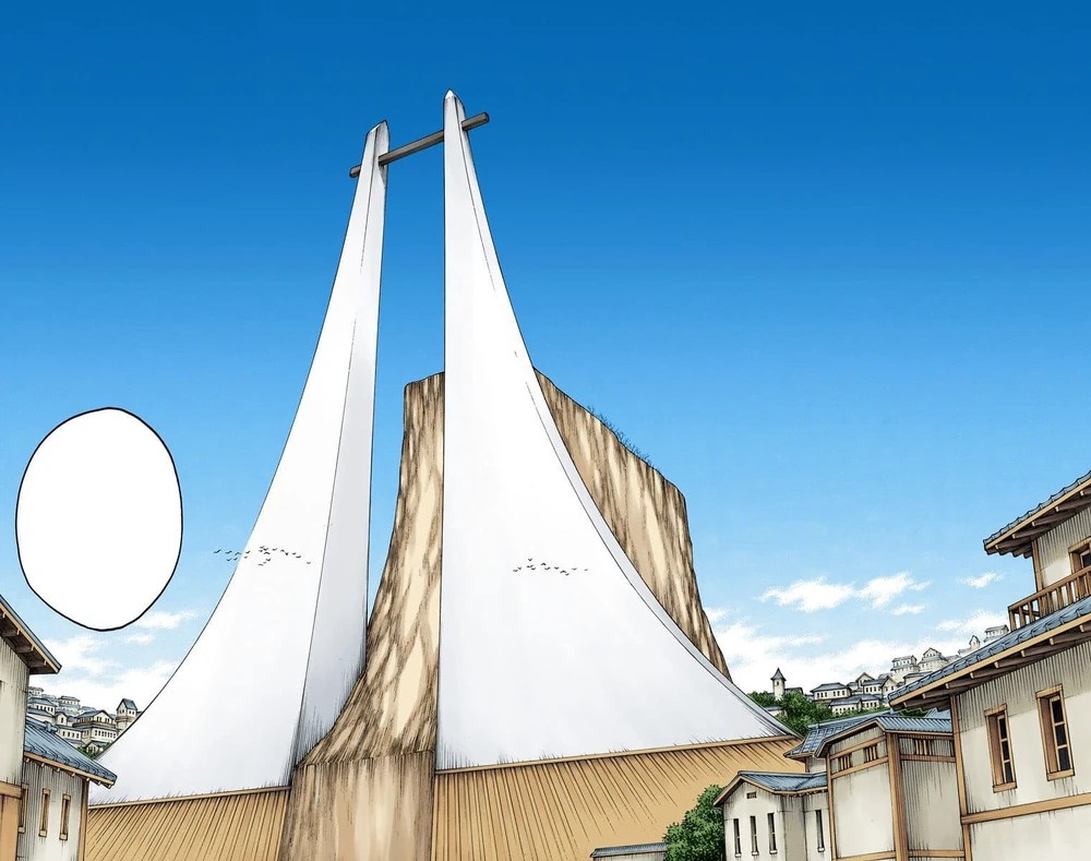 Edifício monumental com duas estruturas brancas e altas, curvadas para dentro, unidas por uma barra horizontal no topo, em um cenário urbano com casas tradicionais e céu azul